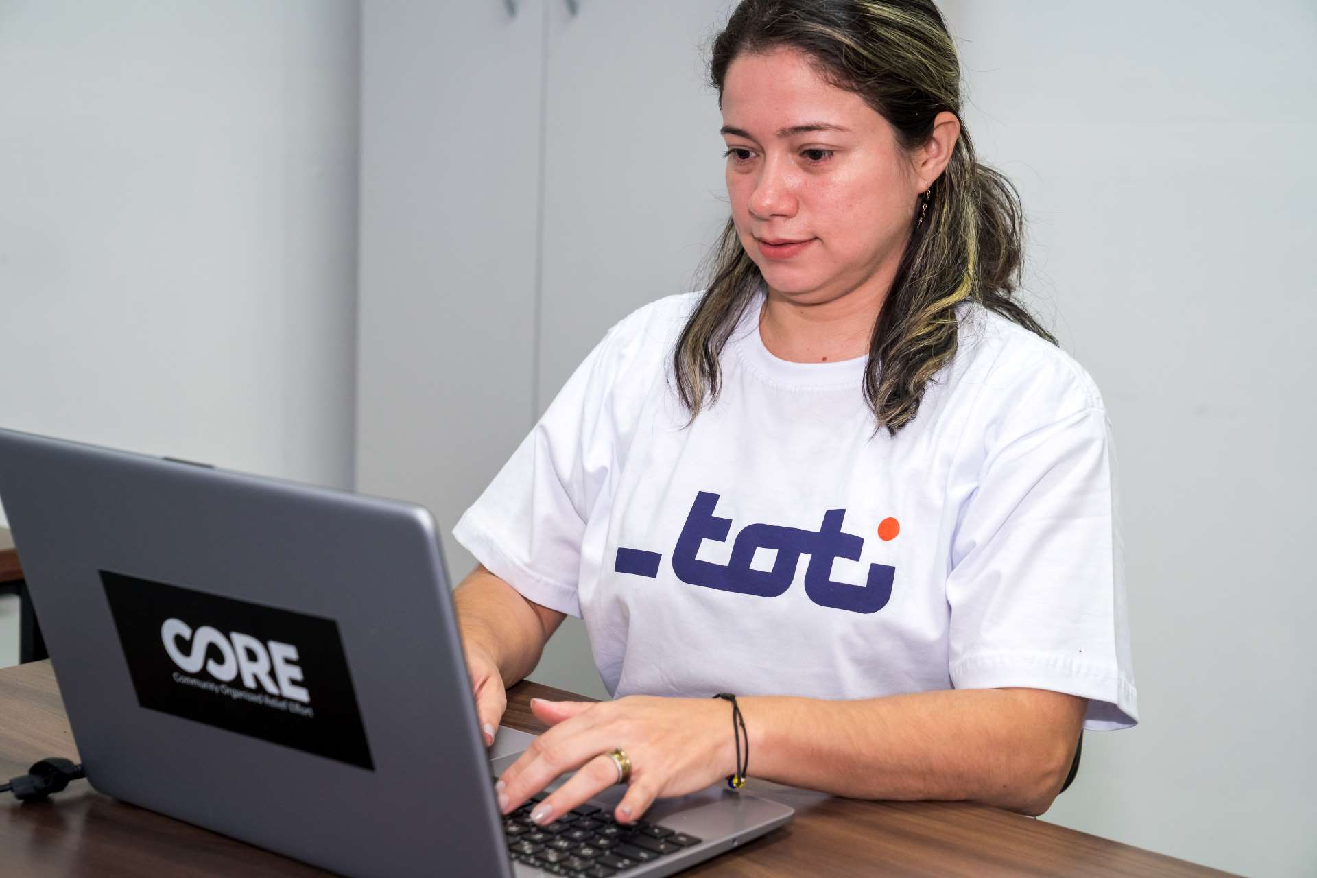 Mulher em camiseta da Toti concentrada em seu laptop em um escritório tranquilo, exemplificando dedicação e foco em suas tarefas.