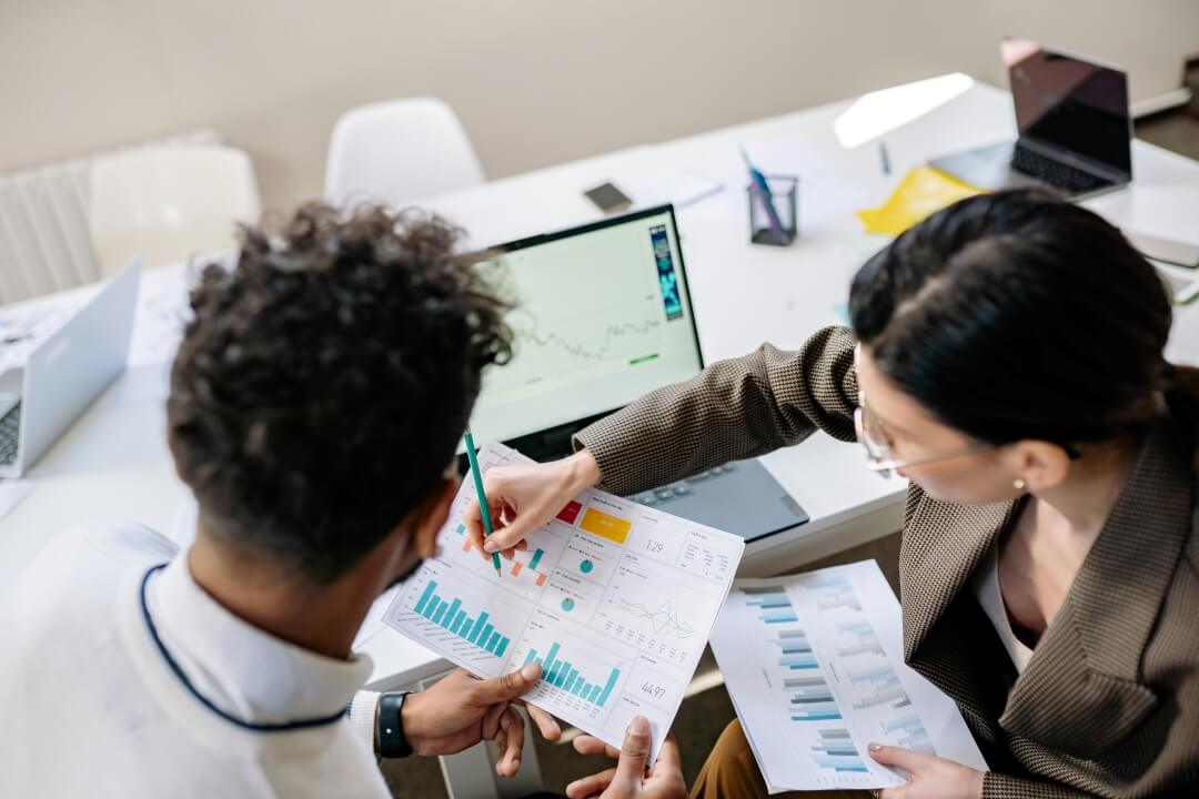 Duas pessoas sentadas à mesa, analisando um documento e conversando sobre os dados.