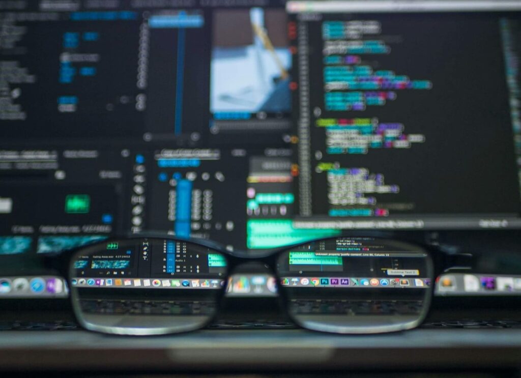 Óculos de grau posicionados em frente a uma tela de computador exibindo um editor de código e uma interface de software