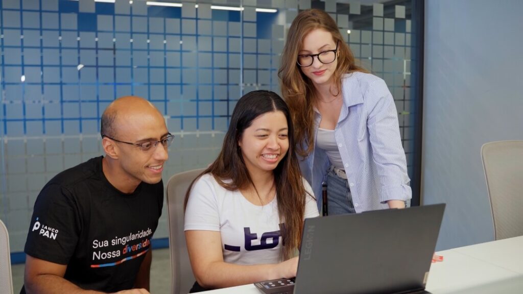 Três pessoas em frente a um notebook trabalhando em conjunto.