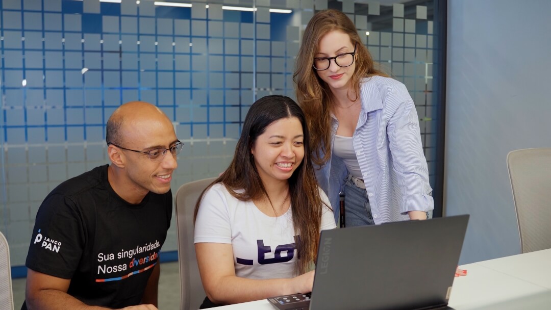 Três pessoas em frente a um notebook trabalhando em conjunto.