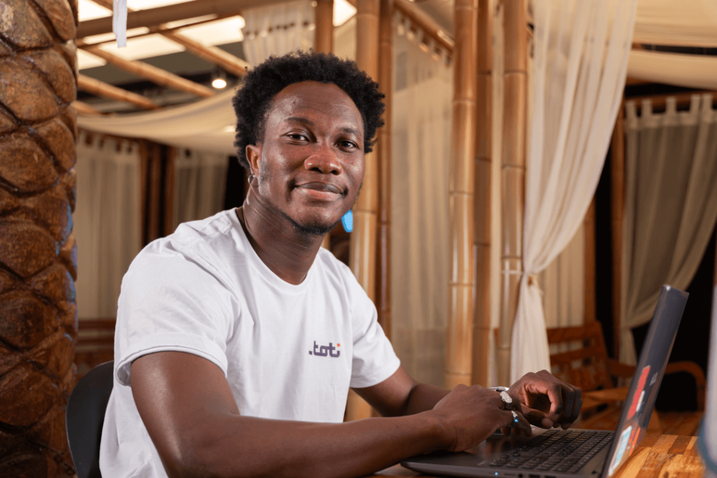 Homem sentado a mesa, vestindo a camisa branca com a logo da Toti